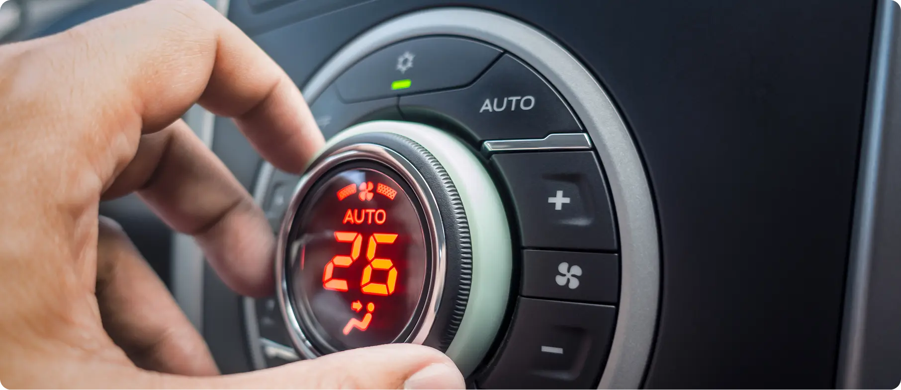 Hand adjusting the automatic climate control dial set to 26 degrees on a modern car air conditioning system inside the dashboard.