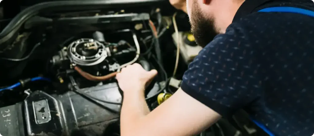 Auto mechanic working on engine components under the hood, inspecting and adjusting parts during vehicle repair in a professional garage.