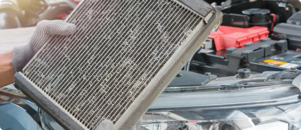 Used cabin air filter being removed from a car engine bay during maintenance, showing visible dirt and buildup on the filter surface.