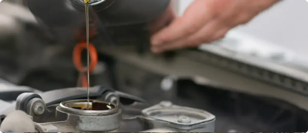 Mechanic pouring fresh engine oil into a car engine during an oil change service in an auto repair workshop.