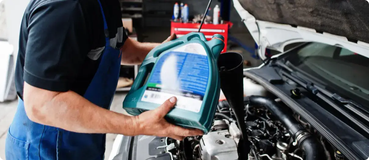 A technician pouring new engine oil from a green container into a car engine.