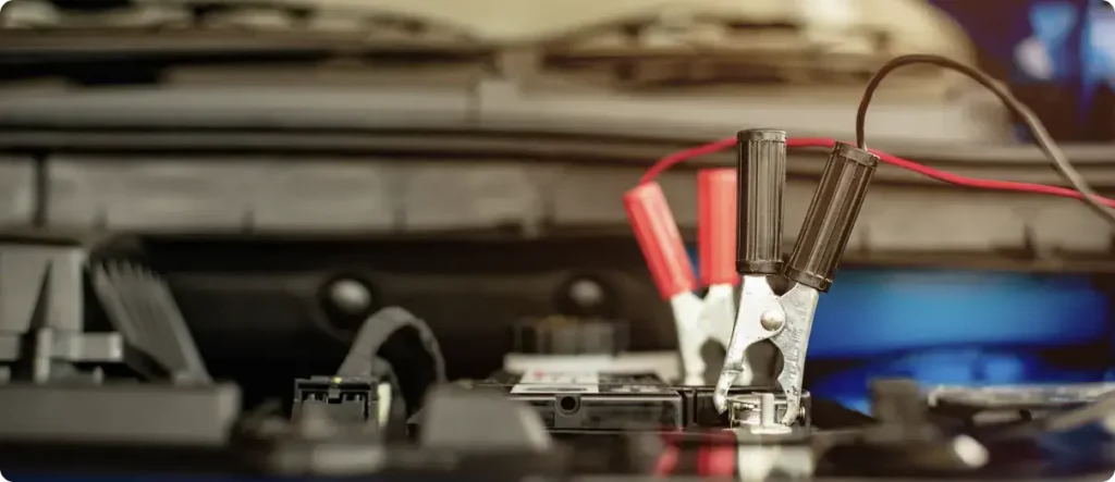 Jumper cables attached to a car battery terminals under the hood, used for charging or jump-starting a vehicle during automotive service.