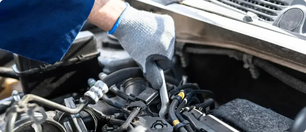 Mechanic wearing protective gloves using a wrench to repair engine components under the hood during professional car maintenance.