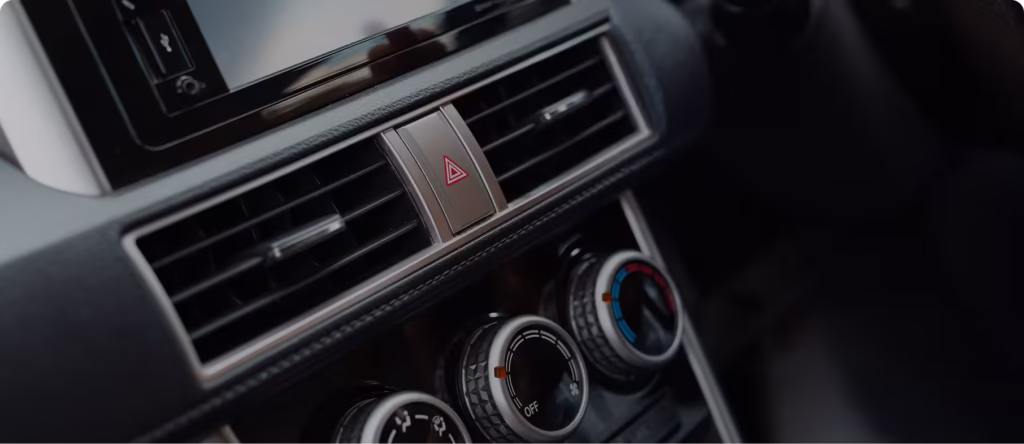 Close-up of a car dashboard center console with air vents, hazard warning button, and climate control knobs inside a modern vehicle interior.