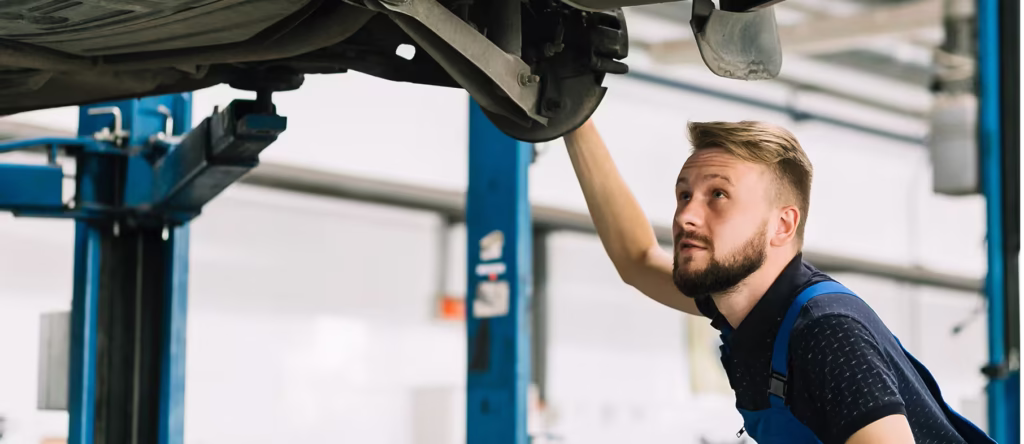 Professional auto mechanic inspecting the underside of a lifted vehicle, checking suspension and exhaust components during a routine service in a modern repair shop.