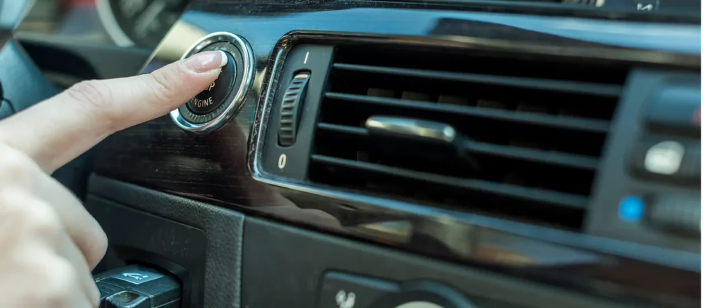 Driver pressing the engine start button inside a modern car, activating the ignition system on a vehicle dashboard.