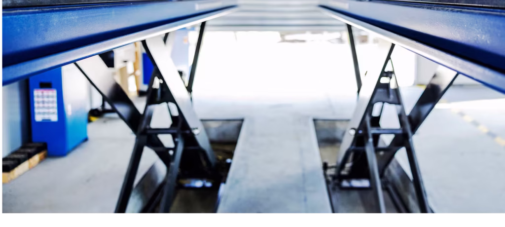 Wide-angle interior view of a professional automotive workshop featuring a heavy-duty blue scissor lift system, ready for vehicle inspection and undercarriage service.
